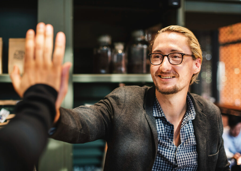 Smiling founder in glasses gives a high-five across a table, capturing the support and momentum a startup mentor Mauritius can bring.